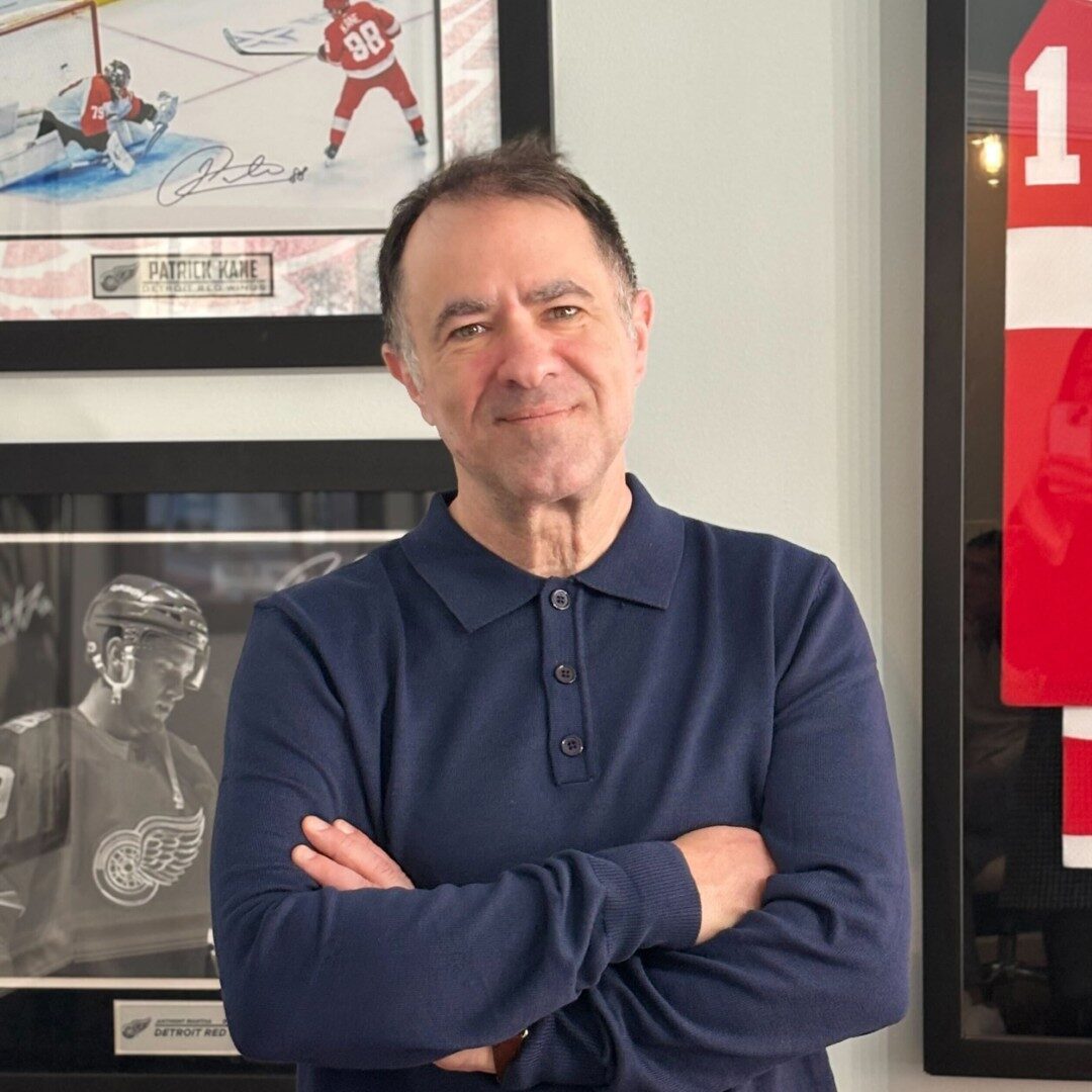 Man smiling in front of framed sports memorabilia.