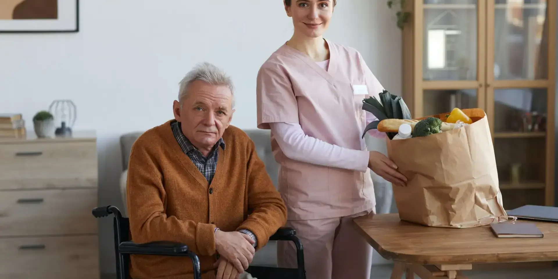 Elderly man in wheelchair receiving in-home care from a friendly caregiver.