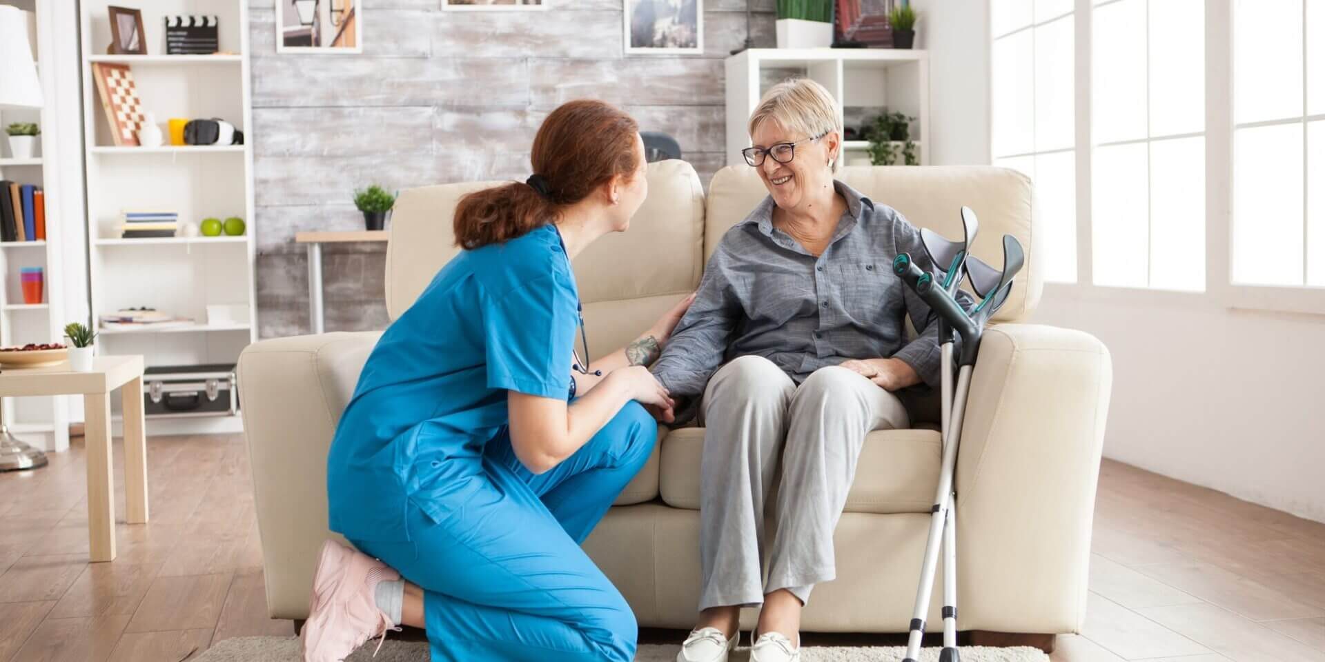 Elderly woman receiving in-home care from a professional caregiver in a cozy living room.